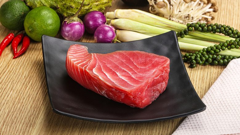 A raw tuna steak on a black plate surrounded by fruits and vegetables