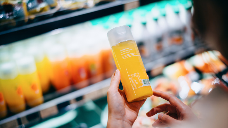 A woman looking at an orange juice bottle at a store