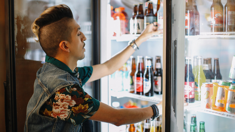 Worker organizing beer bottles in a store fridge