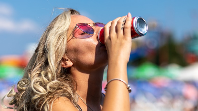 Woman drinking from soda can outdoors in the sun