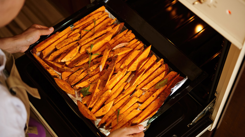 Person putting tray of sweet potatoes into an oven