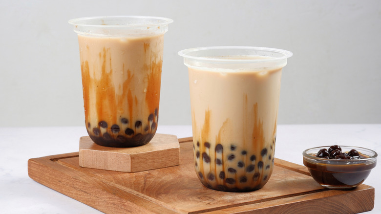 two cups of milk tea with boba on a wooden board