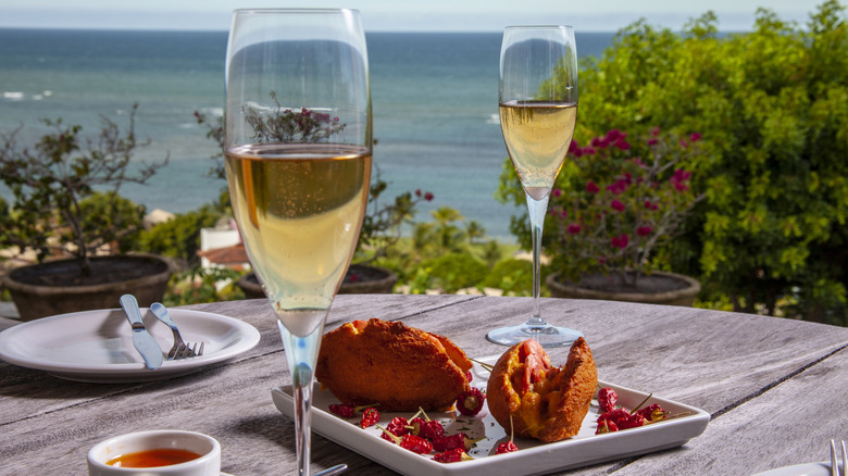 Champagne with fried street food sitting on a wooden table, overlooking the ocean in the background