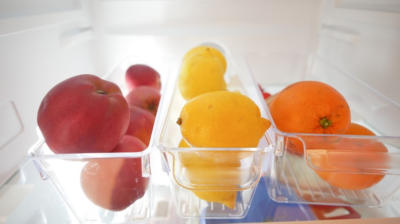 Trays of apples, lemons, and oranges in the fridge