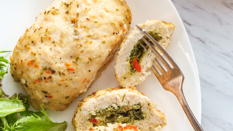 Chicken breast stuffed with artichoke and spinach on white plate with fork and salad
