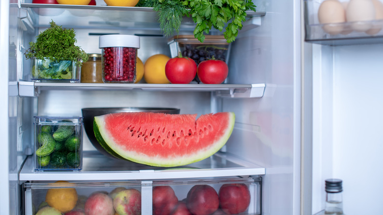 Slice of watermelon in the fridge next to other fruits and vegetables