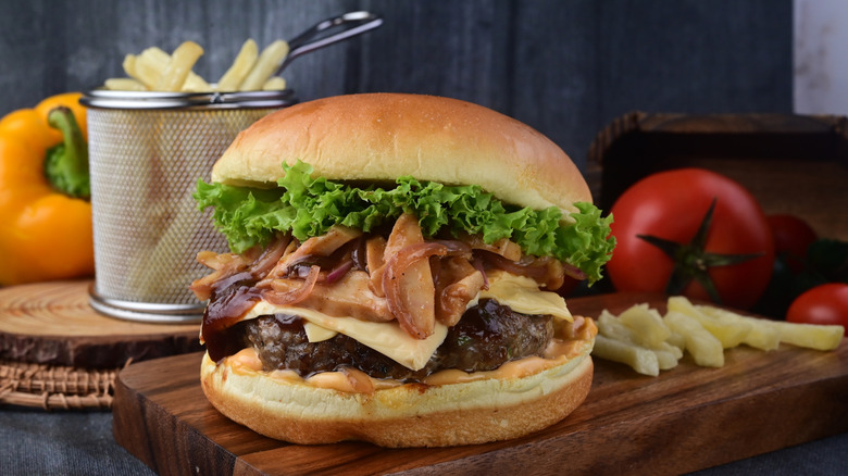 a mushroom Swiss burger on a board with fries and other ingredients in background