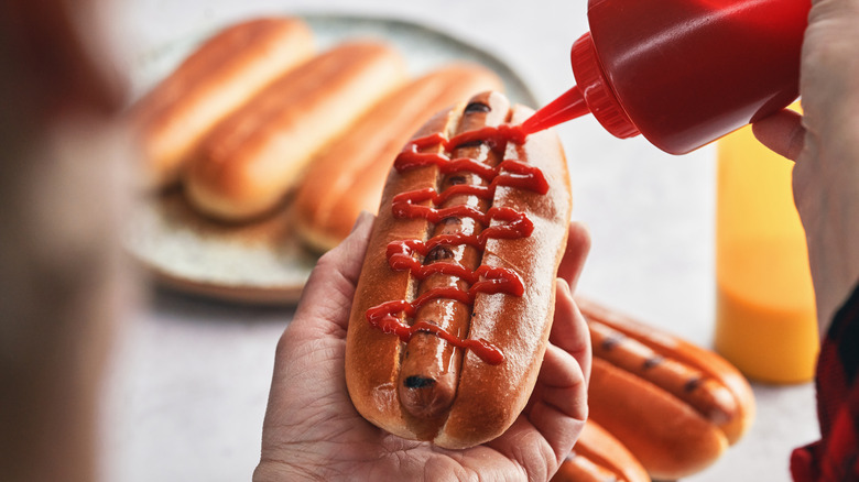 Hand squirting ketchup on a hot dog