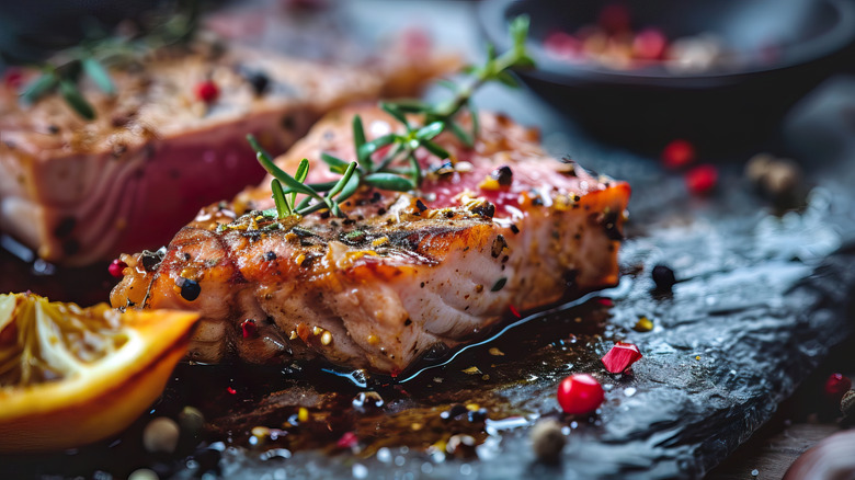 A cooked tuna steak nicely arranged on a cutting board with lemon and rosemary.