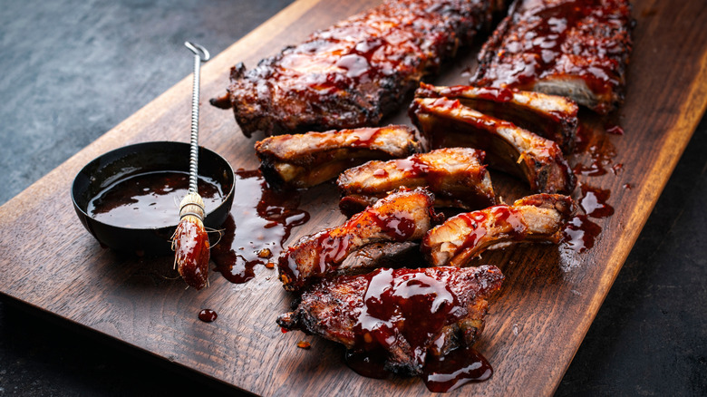 Two racks of barbecue ribs on a wooden cutting board next to a bowl of barbecue sauce