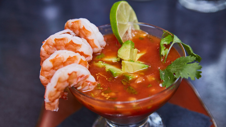 A shrimp cocktail with chunks of avocado and cilantro leaves.