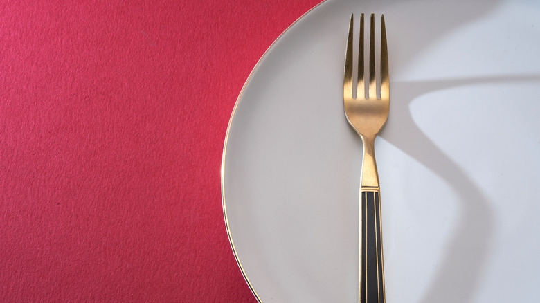 a gold fork on a white dinner plate set against a pink backdrop