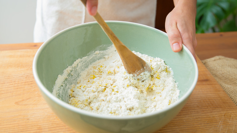 Person mixing dough in a light green ceramic mixing bowl.