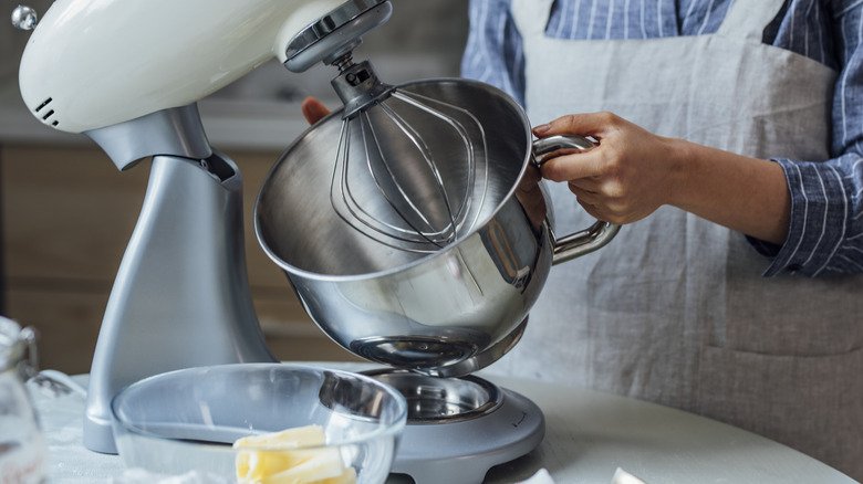 Woman placing stainless steel bowl on stand mixer.