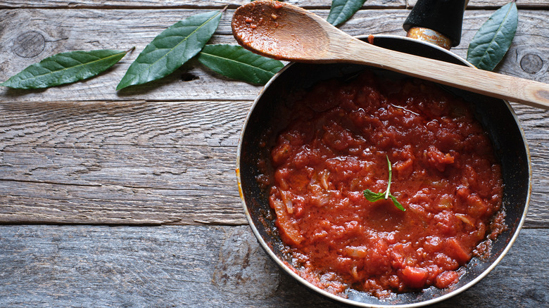 A pan of crushed tomatoes with a wooden spoon against a wooden board