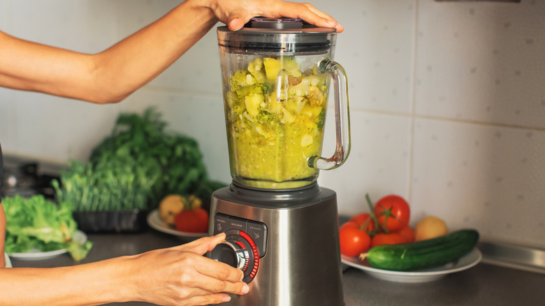 Person using a blender to mix green soup