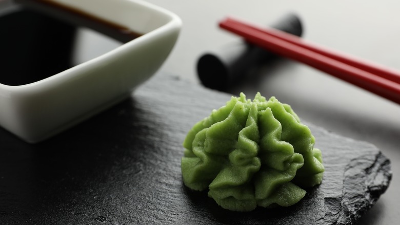A close up of a set of chopsticks, a dollop of wasabi and a bowl of soy sauce.