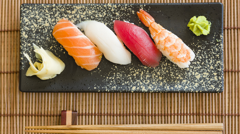 A plate of nigiri sushi pieces with wasabi and pickled ginger on the side.