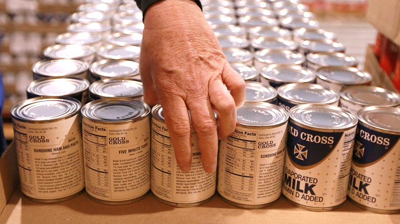 Person's hand picking up canned milk from a grocery shelf