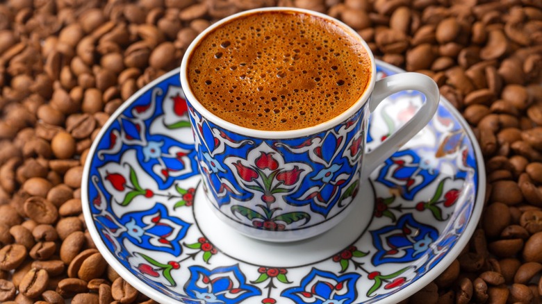 Turkish coffee with foam in cup and saucer and set atop coffee beans