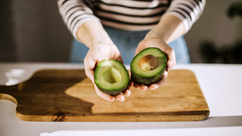 Hands holding a sliced avocado