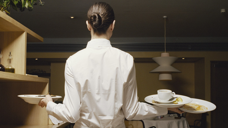 Server in white carrying various plates.