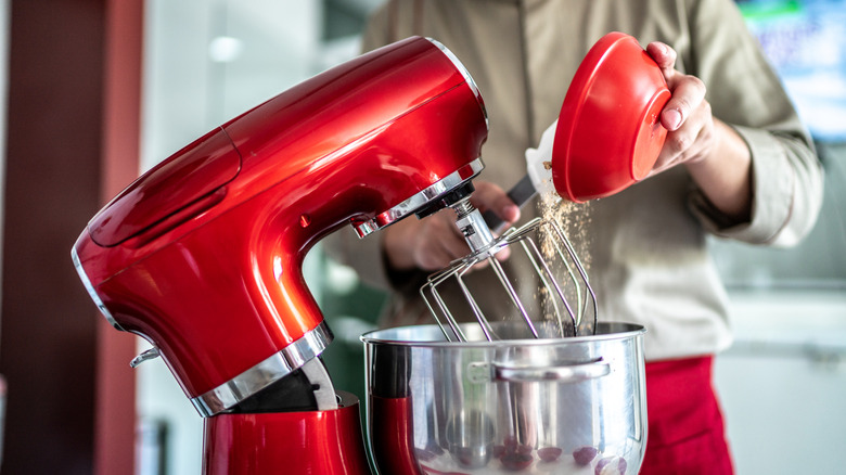 Person pouring ingredients into a red stand mixer