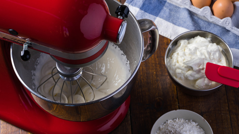 Red KitchenAid mixer on table top with ingredients in bowls on the side