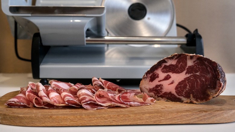 Sliced Italian dried pork on a cutting board with deli slicer