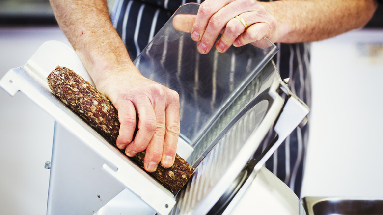 A man using a deli slicer to cut dried sausage