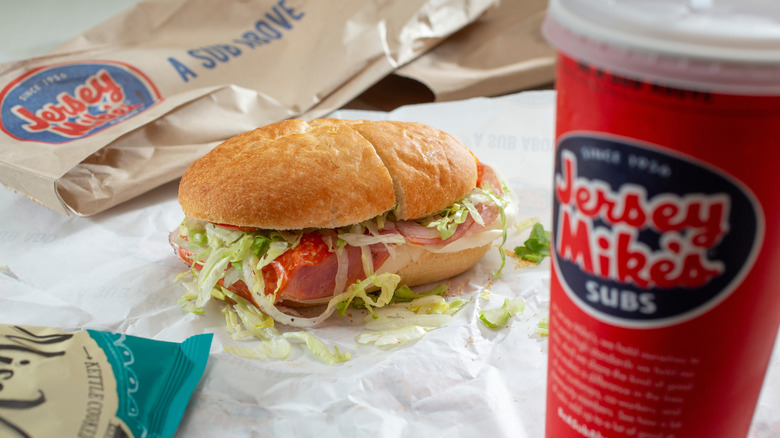 a sub sandwich from Jersey Mike's sits on paper beside a red cup with logo