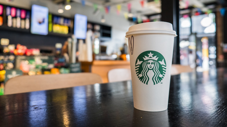 a paper cup of Starbucks coffee sits on a table in the cafe with blurred background