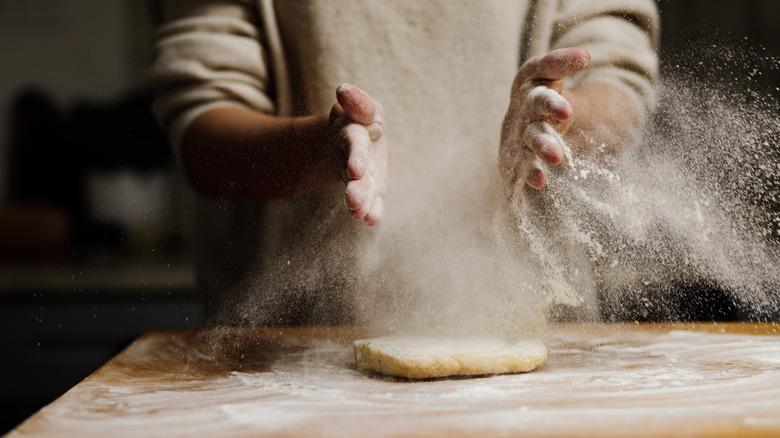 Hands clapping flour over dough