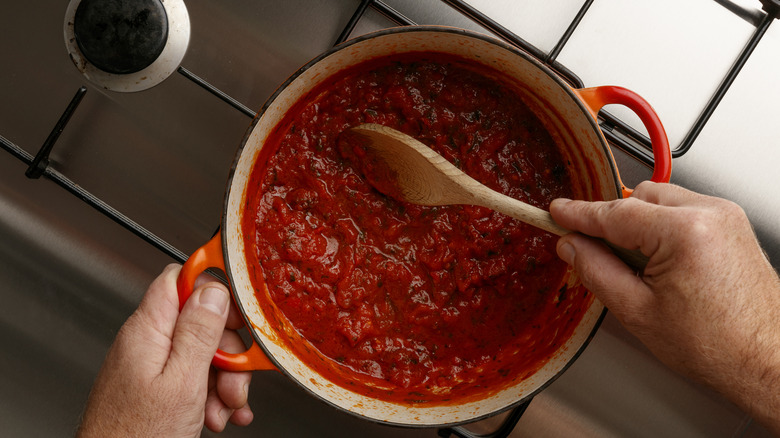 Hands stirring a pot of tomato sauce