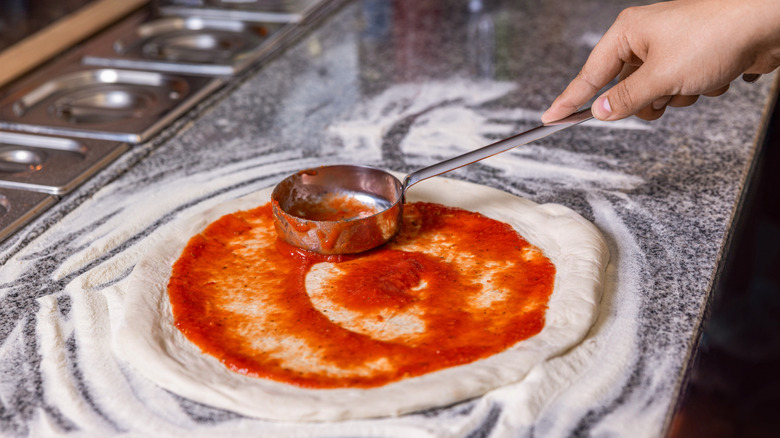 A spoon spreading sauce around on a pizza base