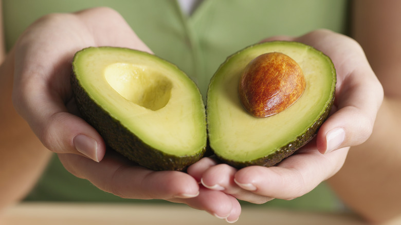 Halved avocado in person's hands