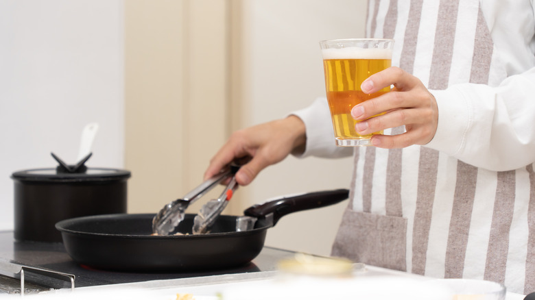 A man holds a beer while cooking