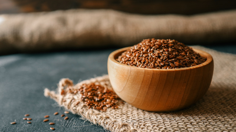 Bowl of flax seeds sits on a woven mat.