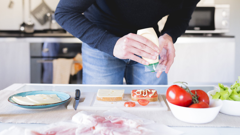 Person squeezing mayonnaise onto sandwich