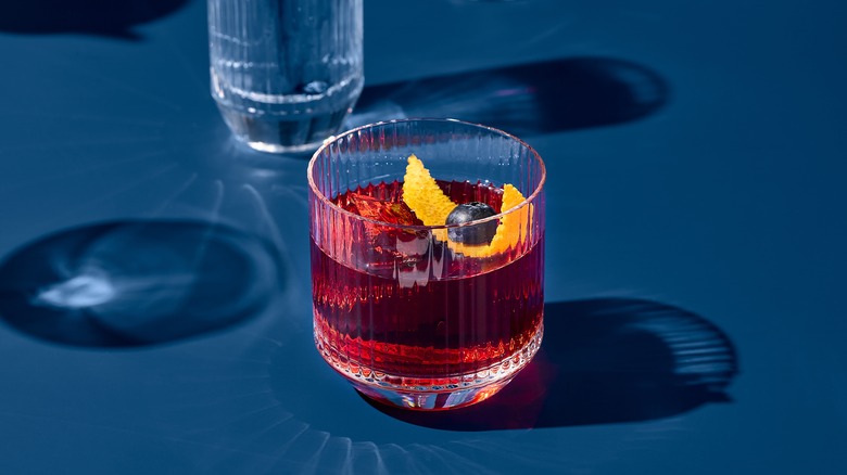 A Negroni cocktail in a glass garnished with orange peel and a blueberry