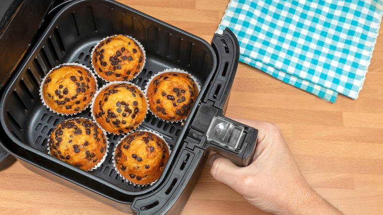 Hand. pulling air fryer drawer out with six muffins