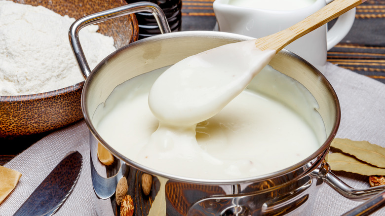 Pot of bechamel sauce with a wooden spoon and sauce ingredients 