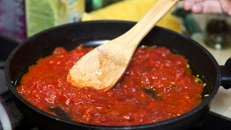 Person stirring iron skillet of tomato sauce with wooden spoon