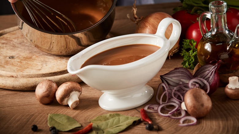 Gravy boat of brown sauce surrounded by fresh aromatics