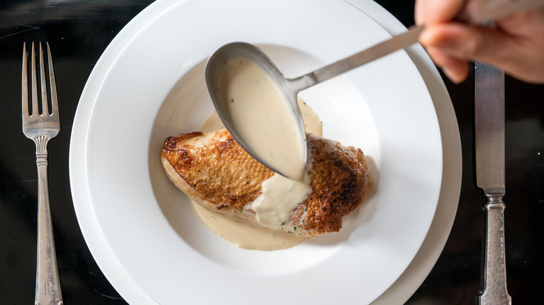 Baked chicken breast in white bowl with ladle of veloute sauce