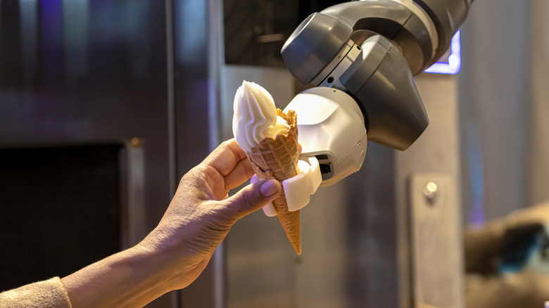 A robot serves an ice cream cone to a human