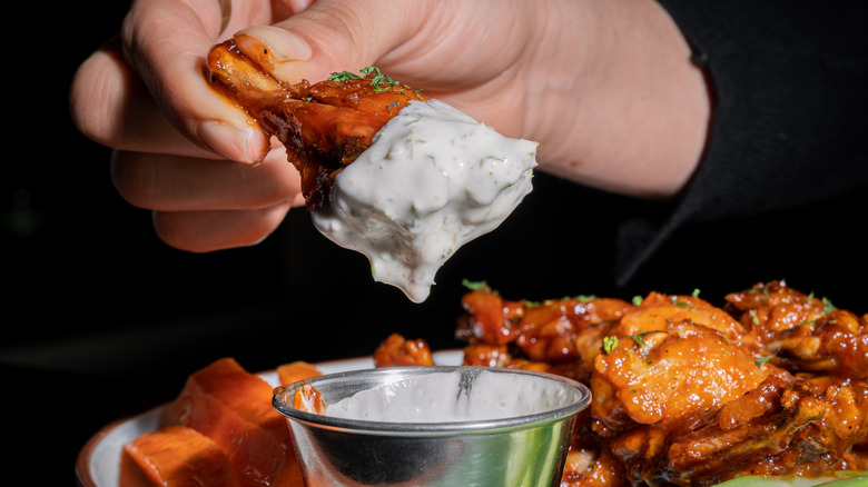 hand dipping chicken wing in sauce