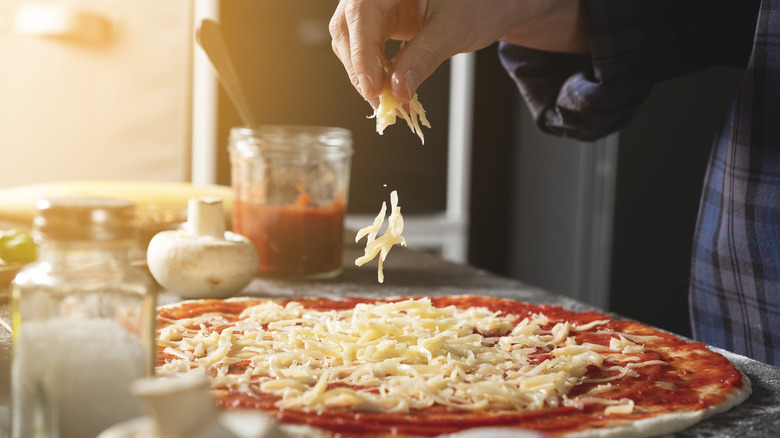 Person adding cheese to pizza