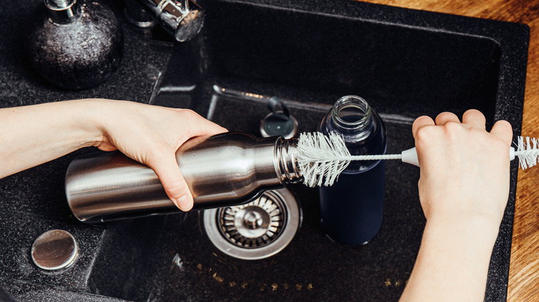 A person's hands wash a reusable water bottle over a sink