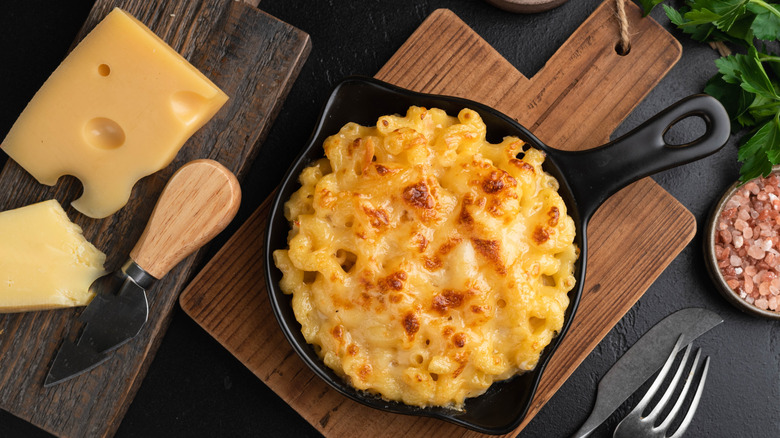 Mac and cheese in a skillet next to cheese on a wooden board